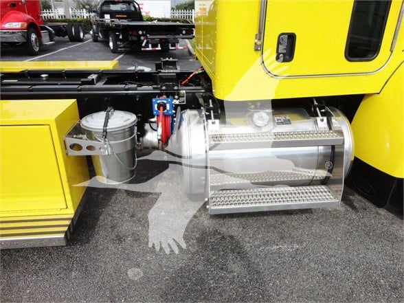 Peterbilt truck side showing stainless steel fuel/steps and auxiliary tank with yellow body. Visible text on metal tank and adjacent components.