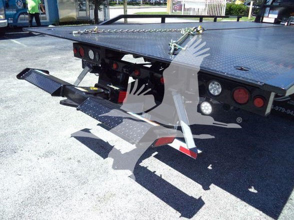 Flatbed tow truck rear with hydraulic ramps extended and taillights visible.
