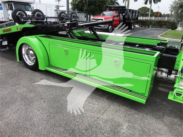 Green Peterbilt 337 tow truck side view with folded wheel lift equipment and service doors visible.
