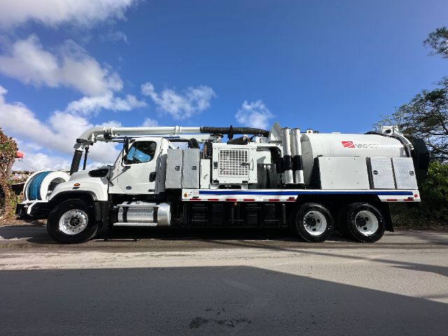 Snow-white Freightliner 114SD vacuum truck side view showing large vacuum tank and hose reel with cab in front.