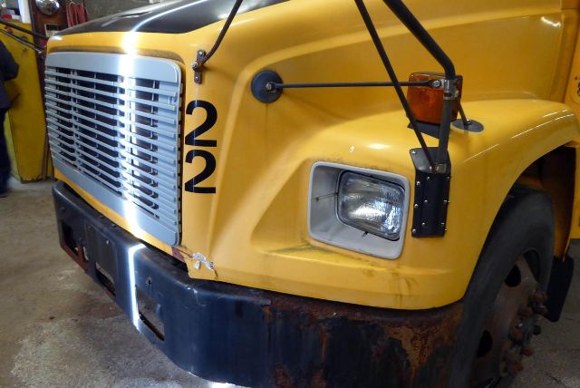 Front-left corner of a yellow Freightliner FS65 bus showing number 22 on the fender, large grille, rectangular headlight, and rust on the lower bumper.