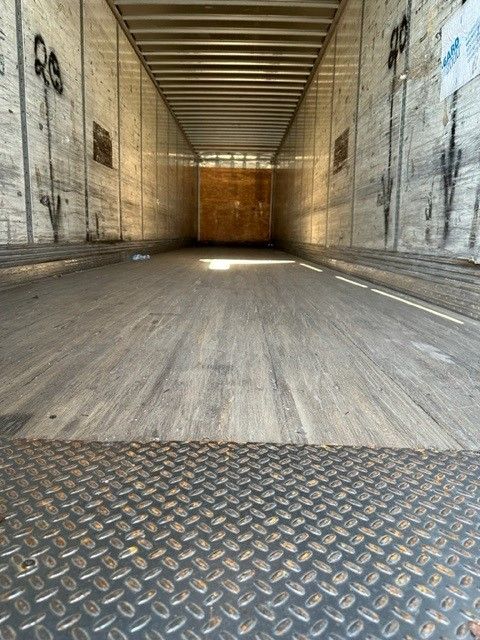 Interior of an empty Wabash trailer with metal walls and diamond plate floor at the rear, large wooden door at the far end, sunlight streaming in.