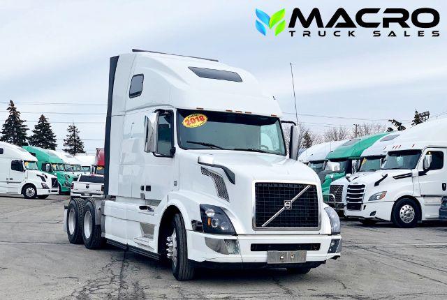 2018 Volvo VNL 670 conventional sleeper truck in a dealership lot with MACRO TRUCK SALES logo in top right corner; white cab, sticker on windshield, multiple trucks in background.