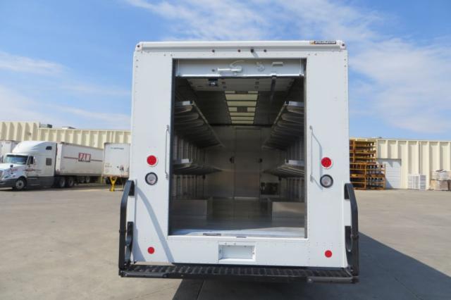 Rear view of a white Ford step van with open cargo area, showing interior shelves and empty cargo space.