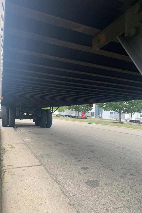 Underbelly view of a Vanguard VXP trailer showing tandem rear axles and underside structure with parked trailers in background.