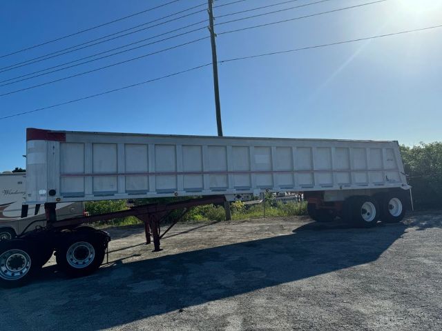Dump trailer long rectangular gray-framed trailer with dual rear axles and a tractor unit at left; no visible branding text legible on the trailer.