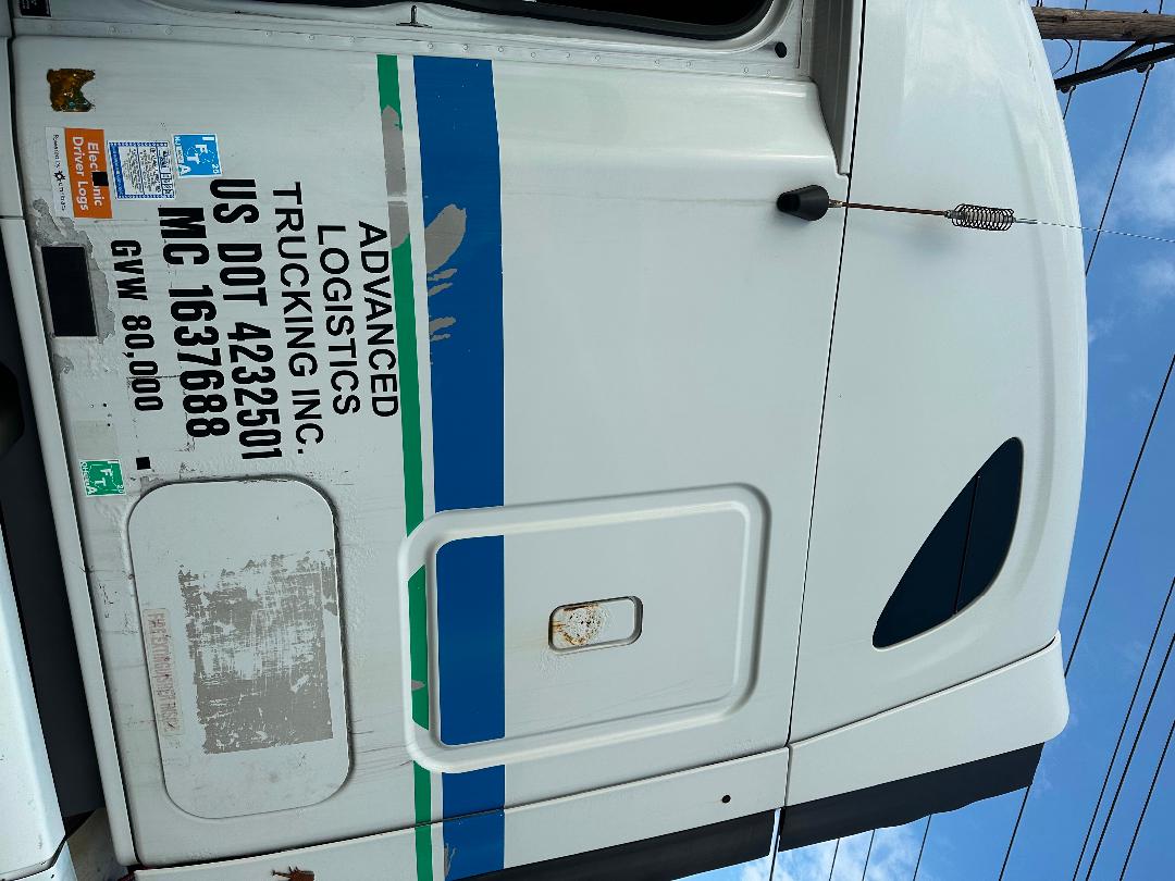 Truck cab door with decals: 'Advanced Logistics Trucking Inc. US DOT 4232501 MC 763768' and blue/green stripe. Front sleeper cab, antenna, door handle.