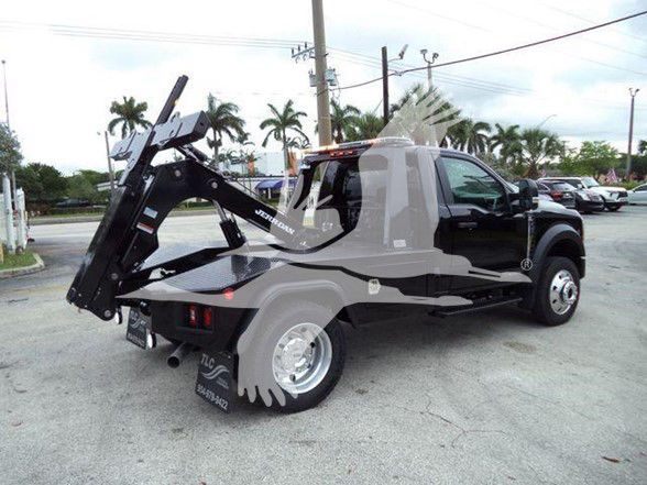 Tow truck with a hydraulic wheel-lift in a black cab, side view showing rear bed and equipment, no visible text legible.