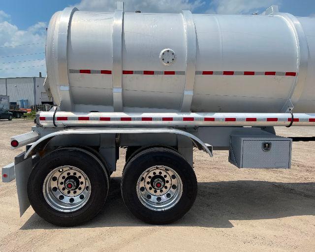 Crude oil tanker trailer mounted on dual rear axles with aluminum DOT-407 tank and reflective stripes.