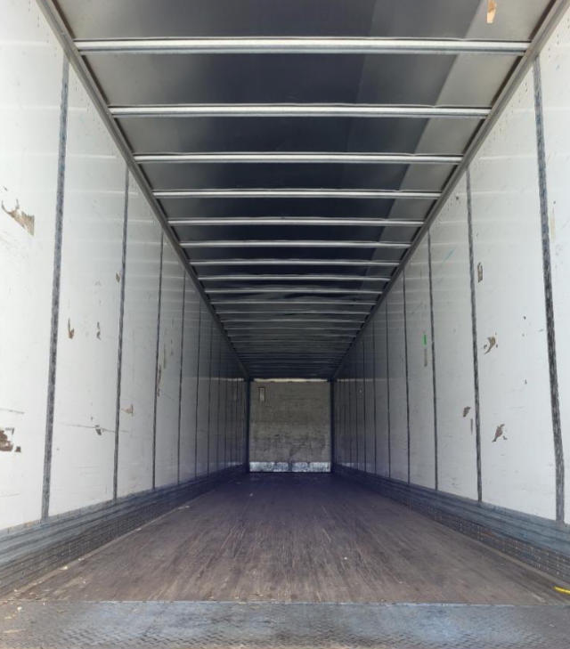 Trailer interior showing empty cargo space with metal sidewalls and ceiling, wooden floor, rear door closed.