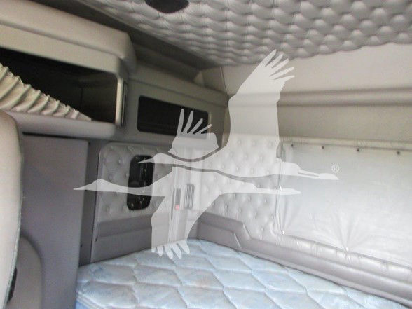 Interior sleeper cab of a Kenworth truck showing a quilted mattress area and side paneling with a small vent-like opening. No legible text visible.