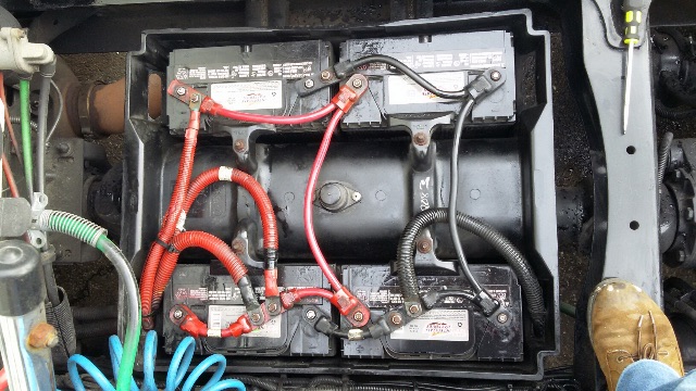 Truck battery compartment with multiple red and black cables connected to two large batteries; visible wiring and hoses in a Freightliner Columbia engine bay.