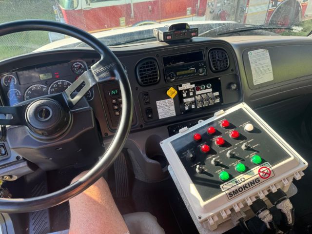 Truck cab interior of a Freightliner 114SD showing steering wheel, dashboard gauges, and a control panel with red and green pop-out switches and labels.
