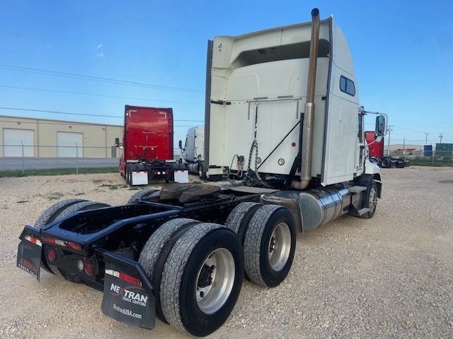 Truck chassis and rear of a 2015 Mack CXU613 sleeper tractor showing triple rear axles, dual fuel tanks, exhaust stack, and fifth-wheel area.
