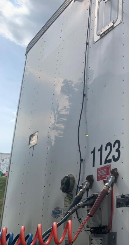 Rear side of a silver Vanguard VXP trailer with numbered 1123, showing fuel/air lines and electrical connectors near the rear door.