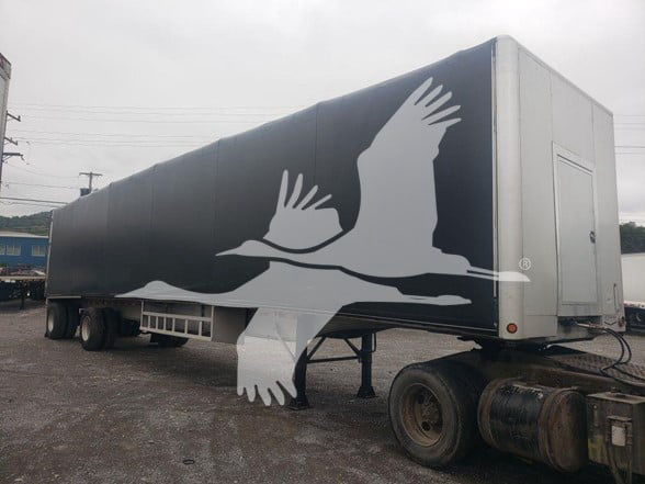 2015 Mac Aluminum flatbed trailer with large white bird graphic on dark gray sides; curtainside model with silver rear end and dual rear tires.
