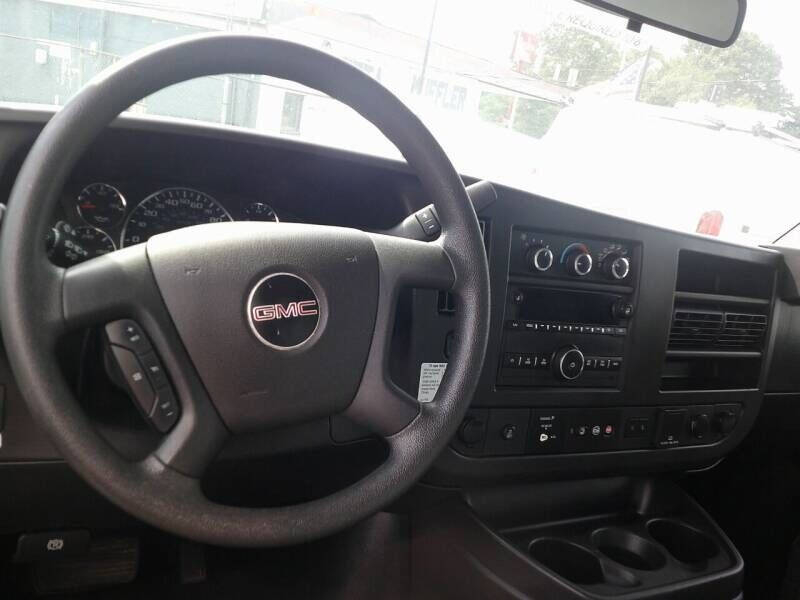 GMC Savana 3500 interior showing steering wheel and instrument cluster. Center console with controls and cup holders visible.