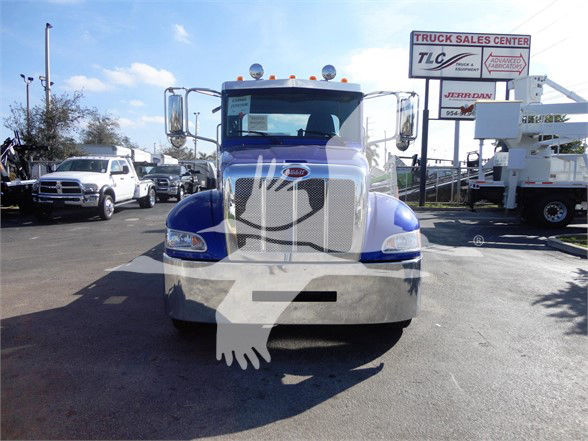 Front view of a blue and chrome Peterbilt 337 truck in a dealership lot, showing grille, bumper, and tall cab with mirrors.