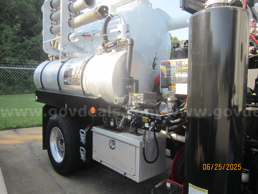 Freightliner Vactor truck with cylindrical vacuum tank and metal toolbox, side view showing control panel, hoses, and warning labels.