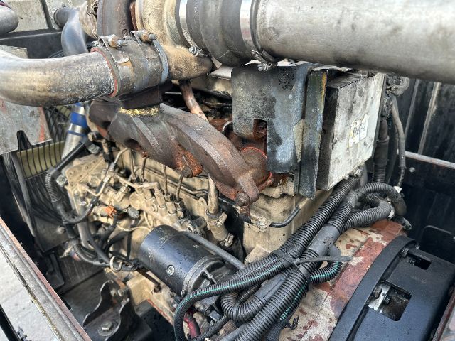 Industrial diesel engine bay with large intake piping, exhaust manifold, wiring harnesses, and control module in a Freightliner M2 vacuum truck.