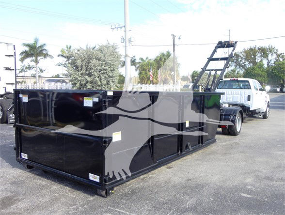 Black dump-style trailer with stylized graphic on side, attached to a white pickup truck in a parking lot.