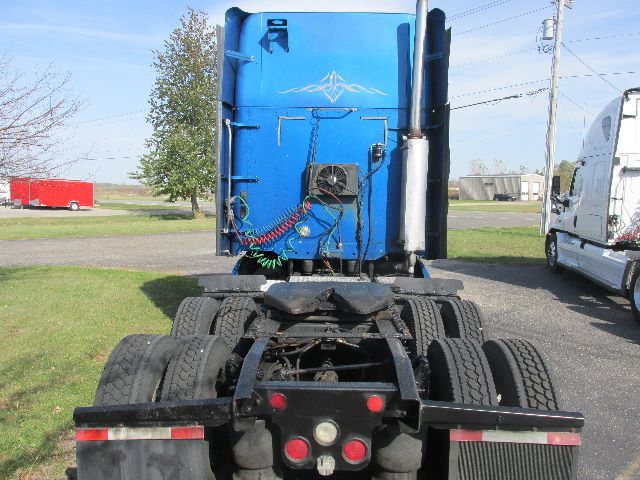 Truck sleeper cab rear view showing blue Freightliner Century cab, fifth wheel, dual rear axles, and electrical lines.
