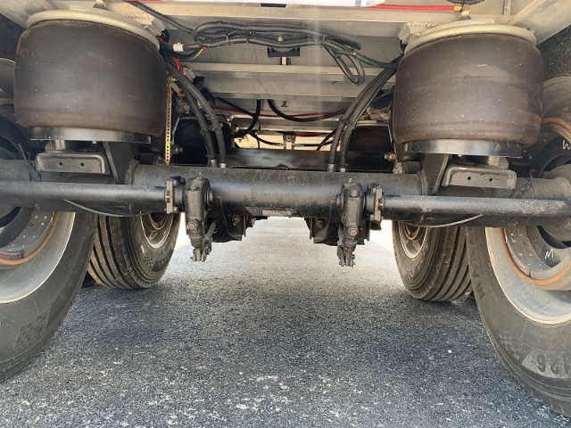Rear underside view of a 2025 aluminum end dump trailer showing the axle, suspension, and leaf springs.