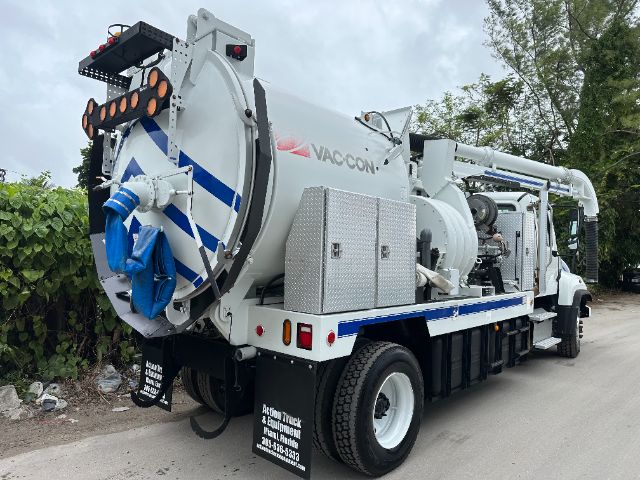 Vacuum truck in service with Vac-Con tank and hose reel mounted on Freightliner 114SD chassis, rear view showing pump assembly and side compartments.