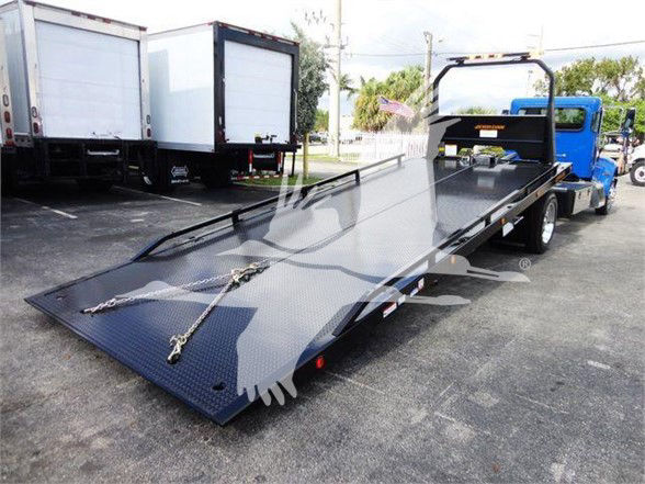 Peterbilt 337 tow truck with a long black flatbed deck in a dealership lot.