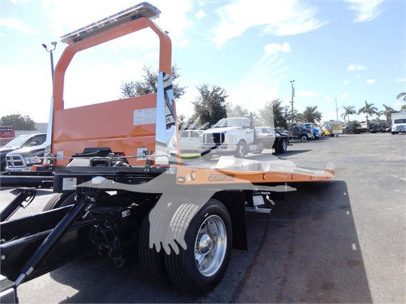 Peterbilt 337 tow truck chassis with a long flatbed and an orange rollover frame on a sunny day.