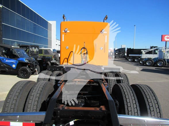 Kenworth W900L tractor rear view showing orange sleeper cab, fifth wheel, dual rear axles, and tires.