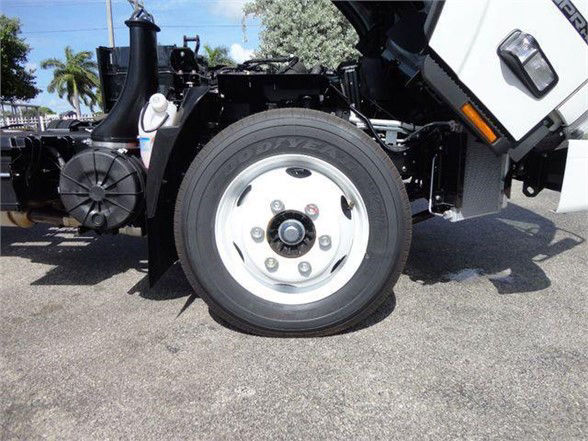 Isuzu NPR HD dump truck wheel and front section showing tire and white steel wheel with hub, chassis components, and white cab door at right.