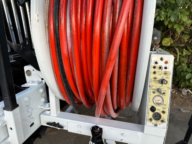 Industrial truck equipment with a large red hose reel mounted on a white frame and a control panel with gauges on the side.
