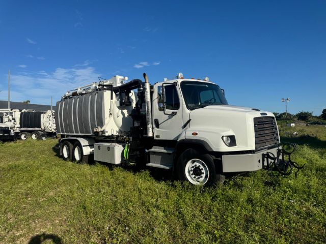 2014 Freightliner 114SD vacuum truck side view showing large rear tank, front cab with dual exhaust and gear attachments, on grassy lot under blue sky.