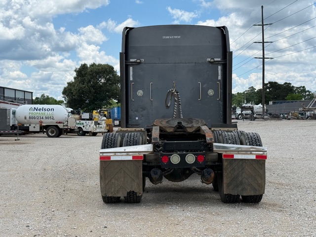 Kenworth W900 rear view showing fifth wheel, dual rear axles, and mud flaps in a gravel lot.
