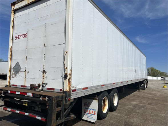 White Wabash dry van trailer with stock number 547108 on rear door, visible rust on frame, dual rear wheels, open area under trailer, blue sky.