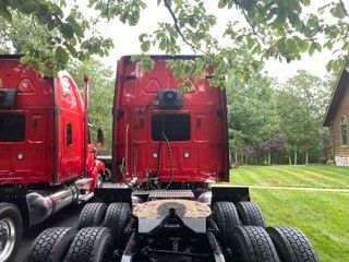 Two red Western Star truck cabs facing away, showing rear and dual rear axles with multiple tires.