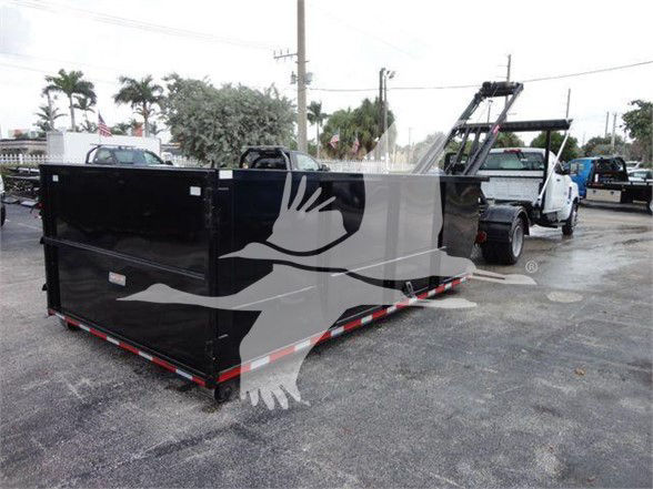 Container truck dump bed in a parking lot with a Silverado 5500HD classified as new. Visible are a large black dumpster bed on wheels with reflective red/white tape along bottom edge and a white tow truck in background.