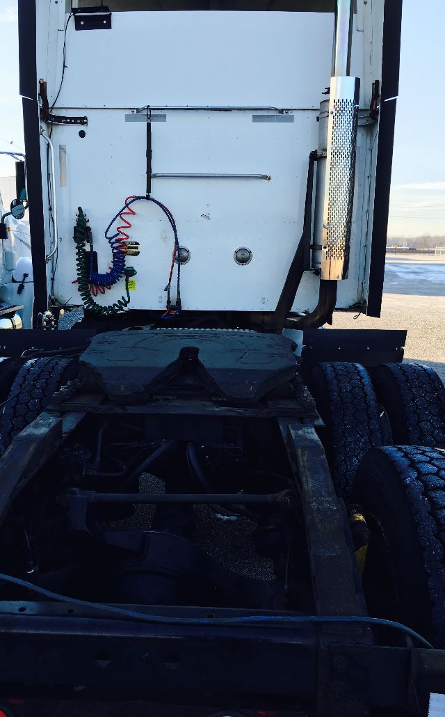 Tractor-trailer cab rear view showing sleeper area with coiled air lines, exhaust stack, and chassis framing.