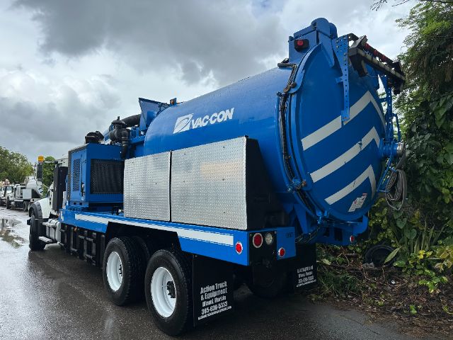 Vacuum truck in blue with Vaccon logo, rear angled, multiple axles, reflective markings, side storage boxes, road on wet pavement.