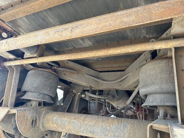 Trailer undercarriage showing suspension air bags, leaf springs, and axles with rust and dirt; structural crossmembers visible.