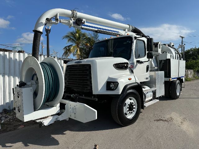 Freightliner 108SD vacuum service truck with large hose reel and front grille, white cab, long rear vacuum equipment, palm trees in background.