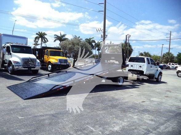 2015 Ford F650 XLT tow truck with a long black flatbed, parked among other trucks; visible front cab and white truck; open flatbed ramp extended.
