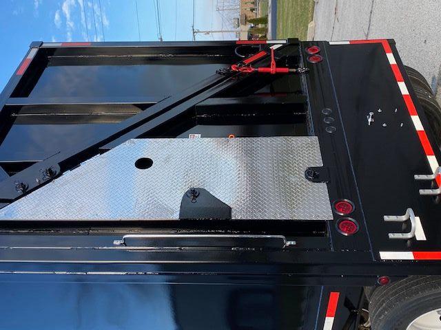Crush car trailer back end showing black steel frame, diamond plate access panel on left, red wheel chock and hydraulic scale, rear lights and reflective tape.