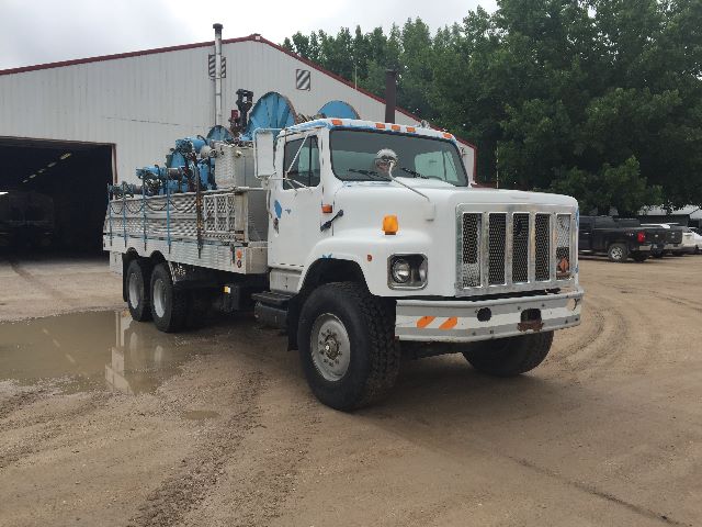 1991 International 2674 service/utility truck with utility bed and equipment mounted on flatbed. White cab, multiple axles, large chrome grille, orange reflectors, stock number 598884 visible in listing context.
