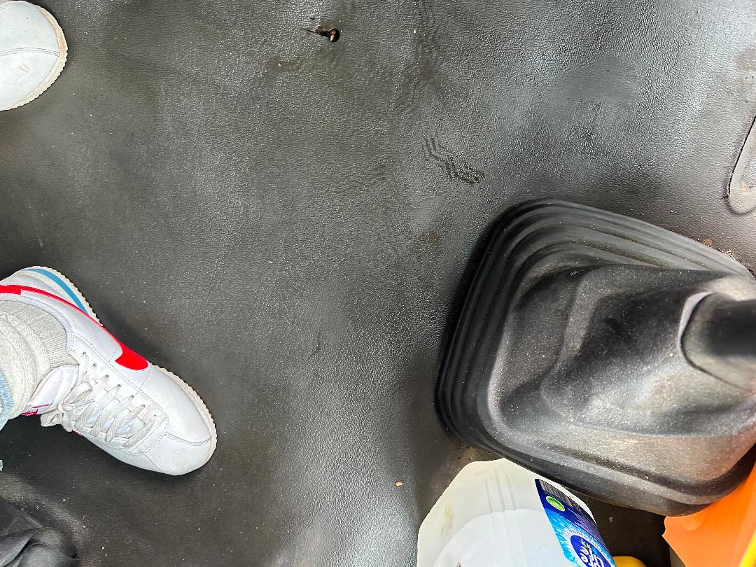 Cab floor of a Freightliner Cascadia truck showing gear shifter boot and surrounding floor area with a cup and shoe visible.