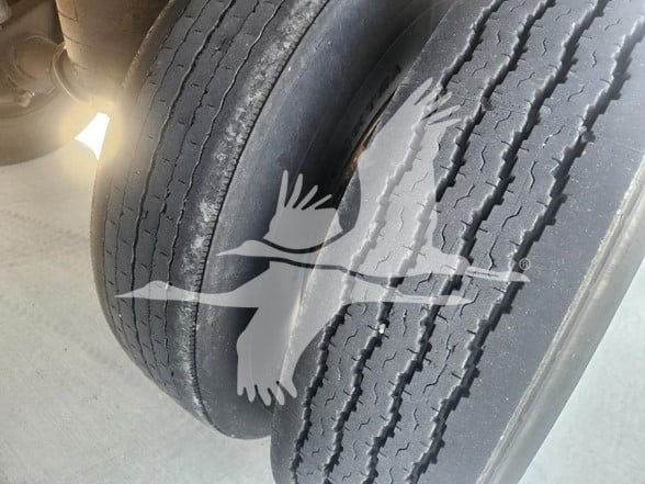 Trailer axle with dual tires and a watermark, no legible labels visible on tire. Some surface texture on tread, no visible branding text readable.