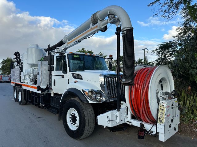 Vacuum truck with white cab and large reel of red hose mounted at front, International 7400 model, long boom hose arm extending over cab, in-service industrial equipment.