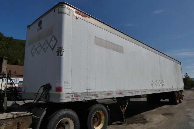 Trailer with white box body on dual rear axles, side and rear decals and VIN-like markings. Visible text includes Great Dane brand logo near front, rear corner markers, and various diamond-shaped hazard placards on the back.
