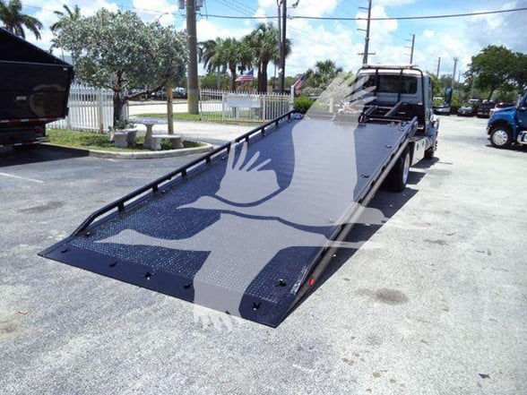 Tow truck flatbed with ramp extended, 2022 International MV in background, stock number T50307.